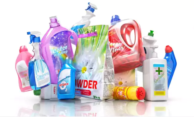 A variety of household cleaning product containers, including plastic bottles, spray bottles, and powder packets for tasks like grease trap maintenance, are grouped together on a white surface. Labels display different colors and branding.